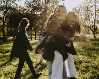 Eine Gruppe von fünf Personen, darunter eine Frau, die auf dem Rücken eines Mannes sitzt und lächelt, während sie in einem Park mit Bäumen und Gras spazieren gehen.